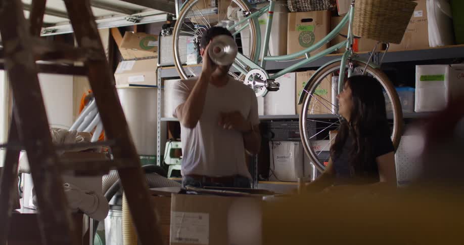 A man and woman are having fun reminiscing in their cluttered garage while looking through old boxes