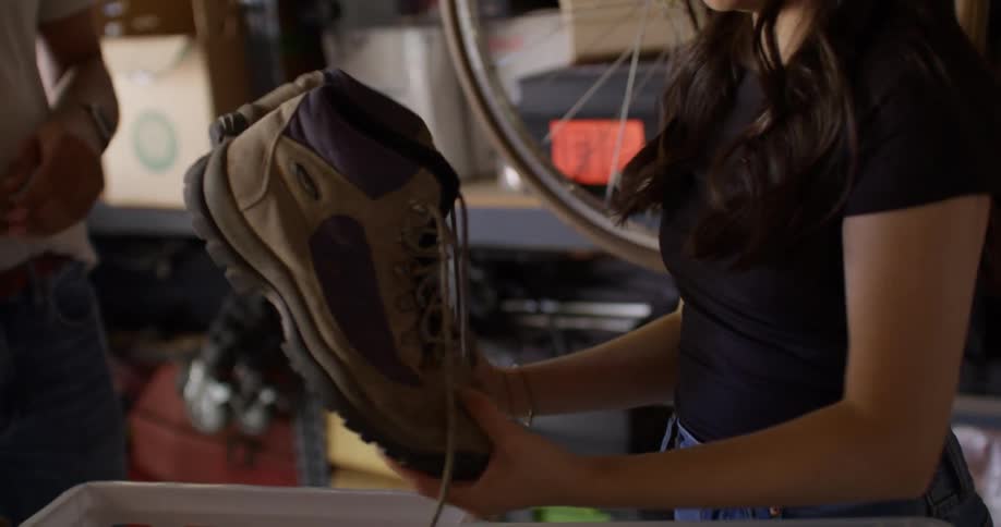 Man handing a pair of boots to a woman who places them inside a plastic box