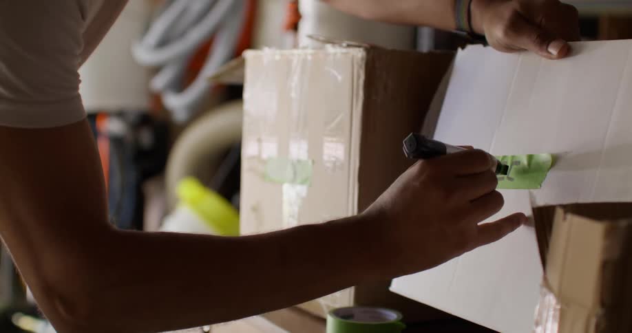 A man wearing a white tshirt writes keep on a box in the garage
