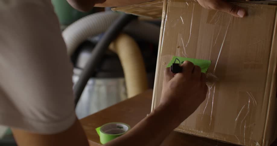 Hands of a person writing on a green ribbon on a cardboard box