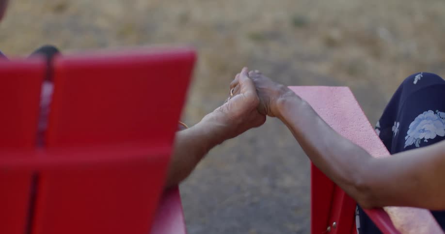 Two people are sitting on red chairs holding hands with one person wearing floralpatterned clothing