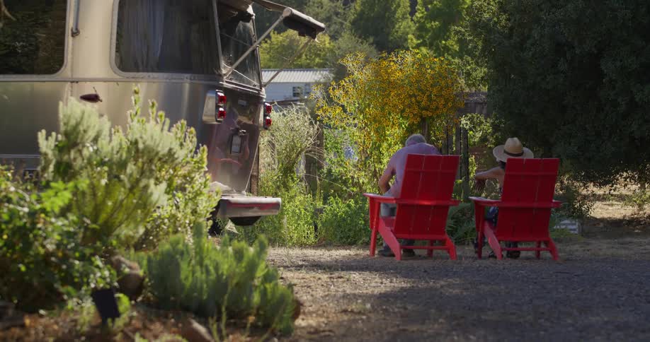 A couple sets up red lawn chairs in front of their silver camper van