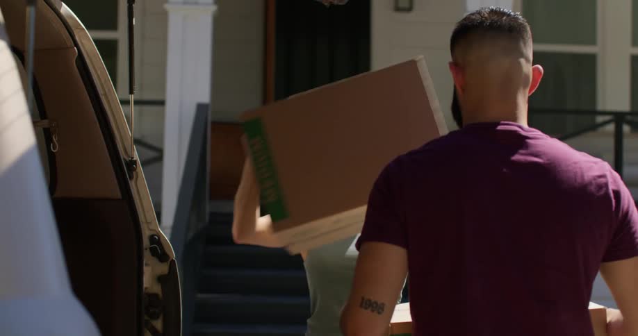 Couple taking moving boxes out of the trunk of a vehicle and entering the house