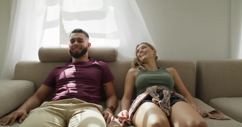 A man and a woman sit on their new brown couch settling into their new home