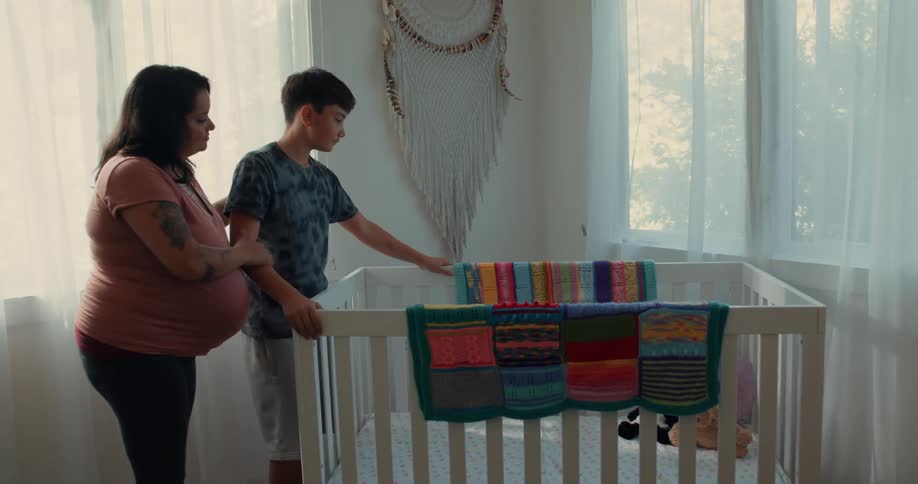 After assembling the crib the pregnant mom and her son huddle close together gazing down at it with wonder