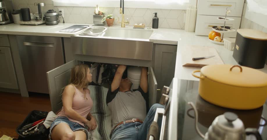 A clip of a plumber fixing the kitchen sink with a lady
