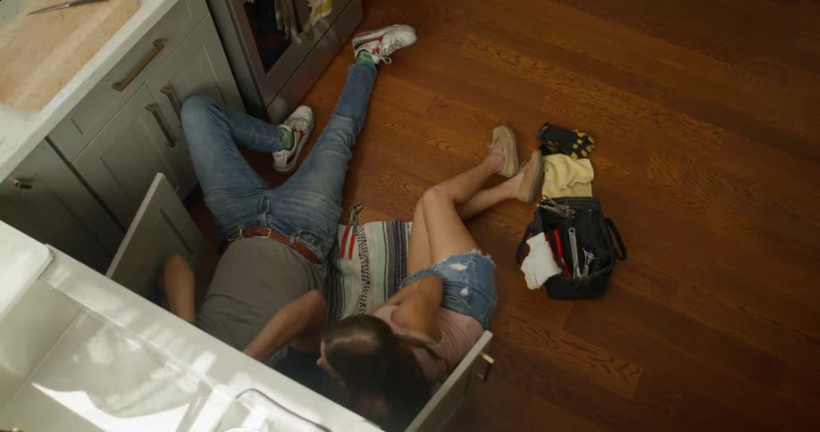 Top view of a man and a woman lying in the kitchen below a sink