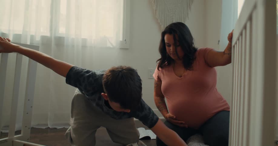 A pregnant woman and a boy assemble a crib