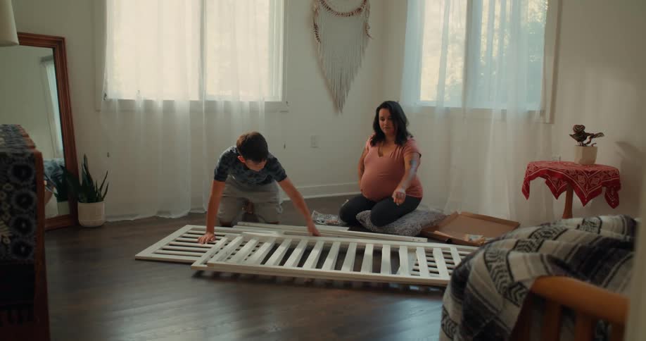 Pregnant mother with her baby in a room setting up a crib