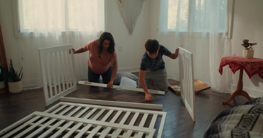 Mother and son are assembling a white crib in a welllit room with wooden floors