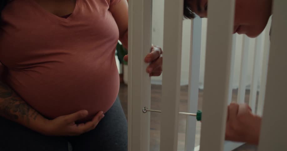 A son uses a screwdriver to assemble the crib while his pregnant mother stands nearby