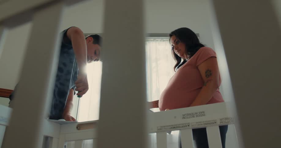 Teenage son helping his very pregnant mom build a crib
