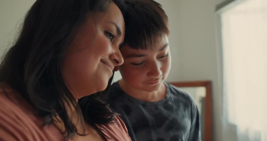 A mother and son are leaning against each other smiling