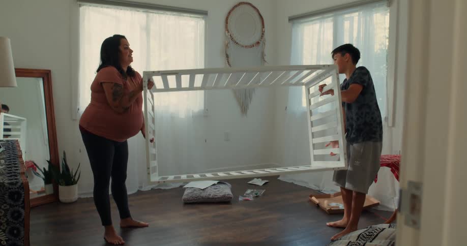 A pregnant mom and her son turn the crib upside down in the room
