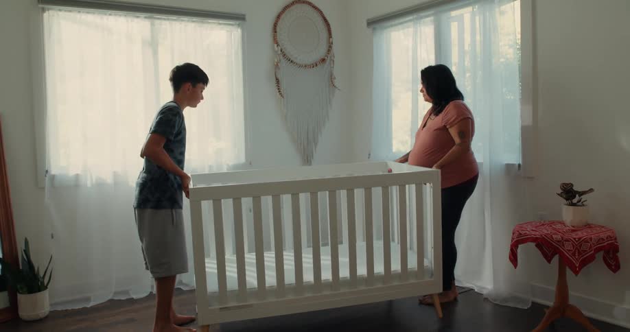 Pregnant mother with the help of her son placing a crib in a room