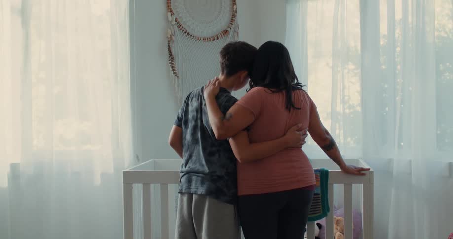 A pregnant woman and a boy stand next to a crib and hug