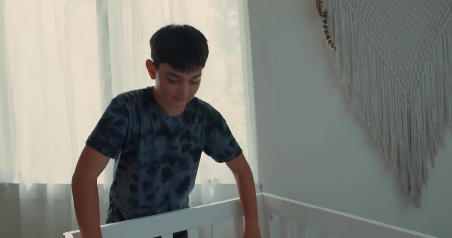 Pregnant mother with her son helping to put a sheet on a crib