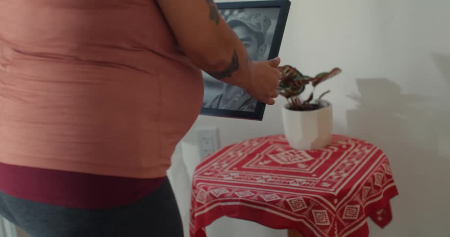 Pregnant woman placing picture frame of man in military uniform on a small table