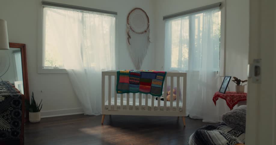 A bright and airy nursery with a white crib a colorful quilt and a dreamcatcher hanging on the wall