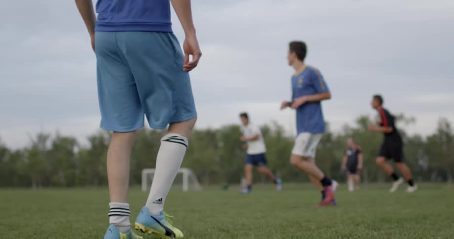 A young man in blue walks backward across a soccer field