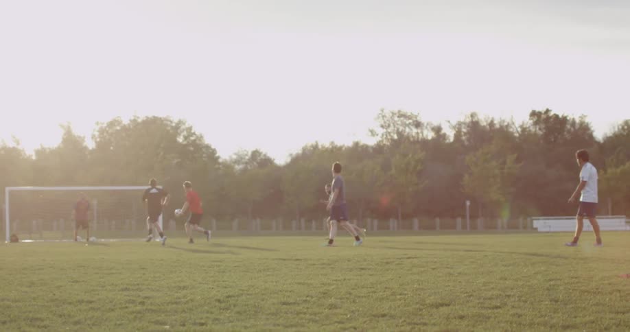 Men are playing a soccer match on a field during late daytime