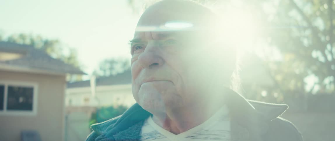 Elderly man looks around while standing in his backyard on a sunny day