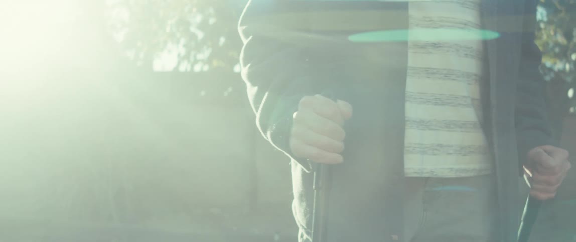An elderly man using canes walks in the backyard on a sunny morning