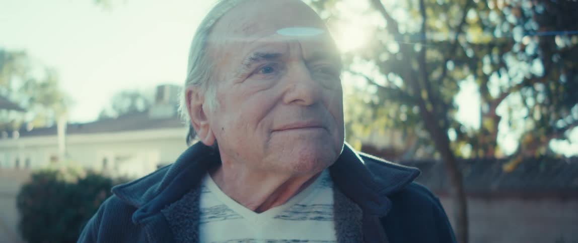 An elderly man standing on the backyard on a sunny morning