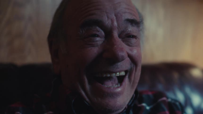 An elderly man in a plaid shirt laughs heartily
