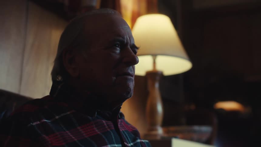 The face of an elderly man who is sitting on a sofa and is saying something while staring straight ahead with a look of surprise