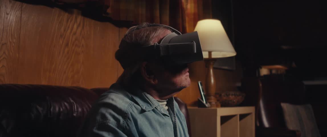An elderly man sits on a couch at home using a virtual reality headset