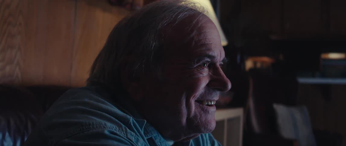 Elderly man smiles while playing a video game with a television at night