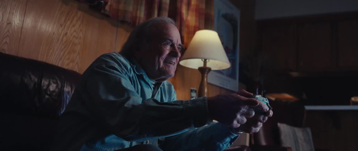 Cheerful elderly man sitting in living room playing video game with wireless remote control