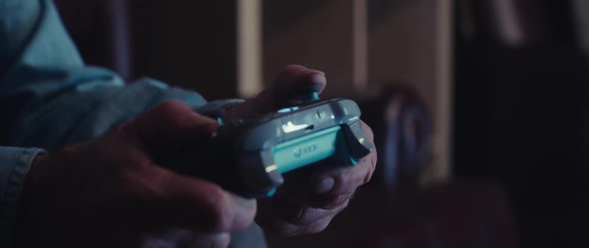 An elderly man is holding and using a video game controller focusing on the buttons and triggers