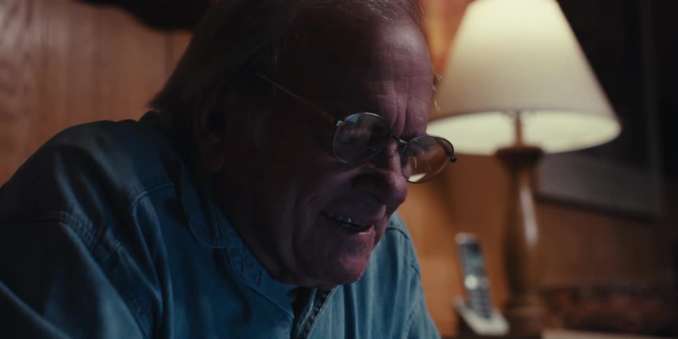 An elderly man at home puts on glasses to use a laptop