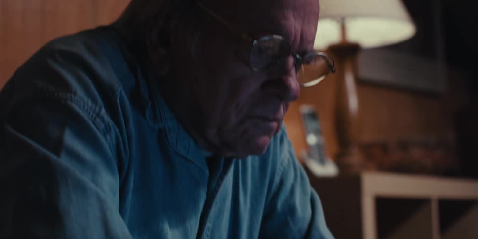 An elderly man wearing glasses is typing on a laptop and looking intently at its screen