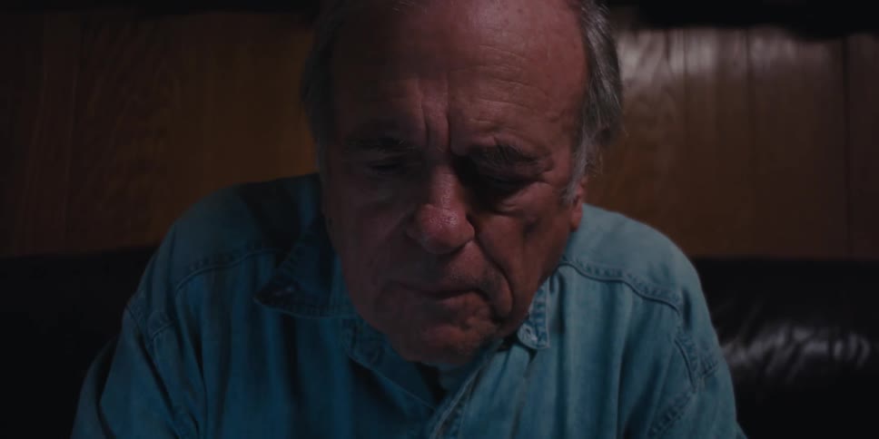 An elderly mans hands typing on a keyboard in a dimly lit room
