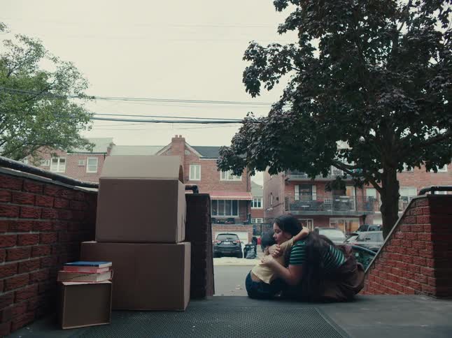 A woman and child sit on the steps of a building with moving boxes talk then hug