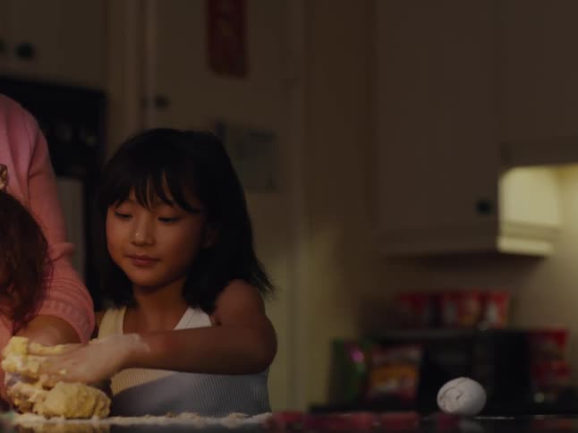 A girl helps her mother make dough in the kitchen at home