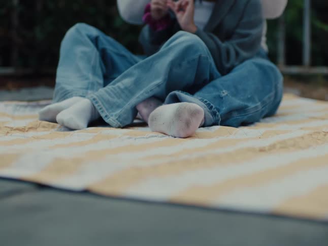 Legs of two people sitting on a yellow and white cloth on the wall