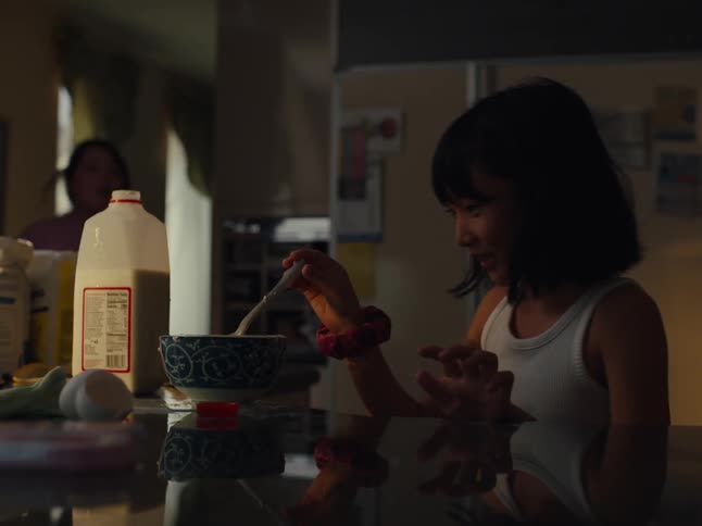 A girl pours milk into a bowl of cereal and it overflows