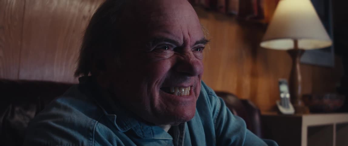 An older man with a blue collared shirt watches something with an intense grimace