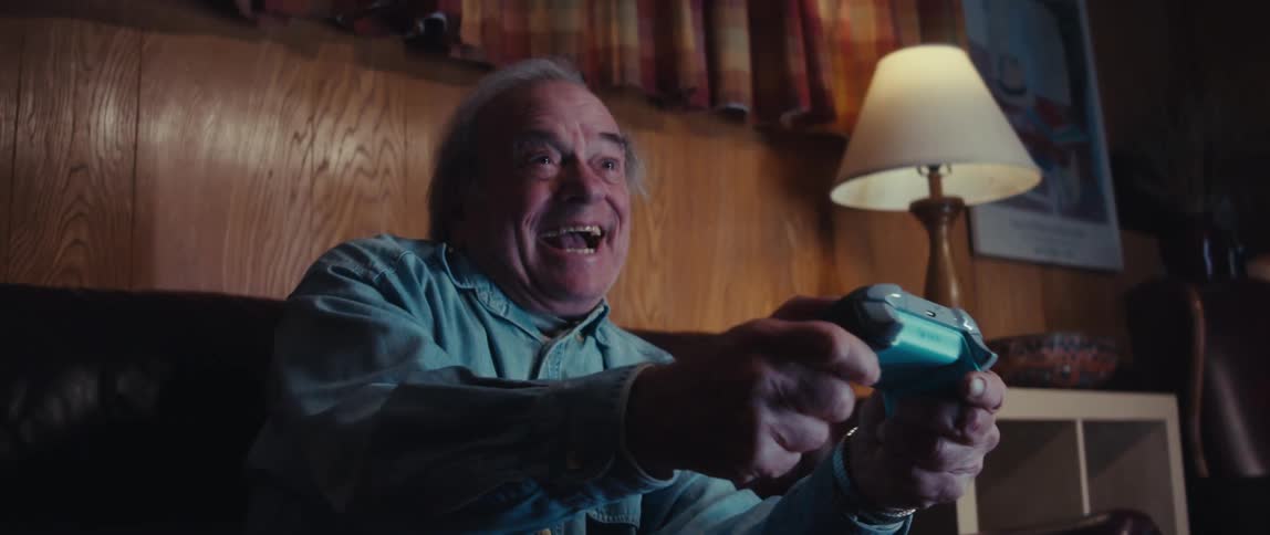 An elderly man is sitting on his couch and smiling while playing video games