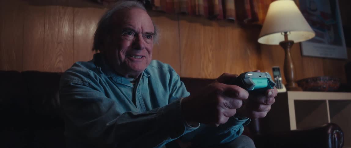 Elderly man sitting holding a video game controller playing