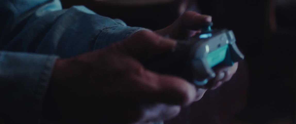An older man in a blue shirt uses an xbox controller then smiles and laughs