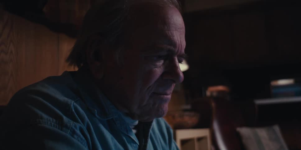 An elderly man sitting at home in a dimly lit room