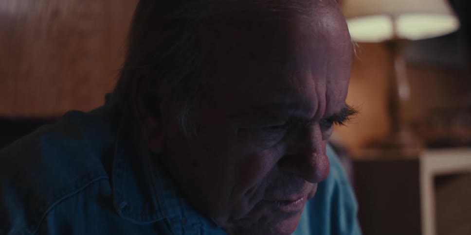 Close up of an elderly man writing on a notebook in a dimly lit room