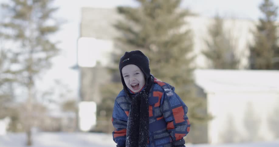 A young boy wearing a snowsuit laughs outside