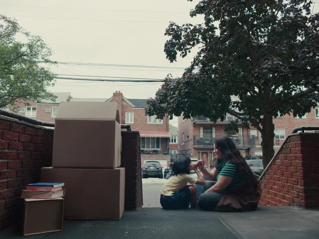 Mother and daughter sitting on the steps outside a building surrounded by cardboard boxes and books