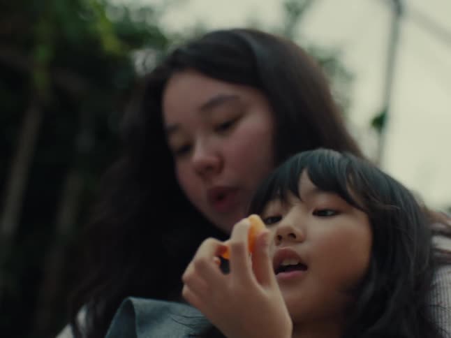 Mother and daughter sit close together eating orange slices